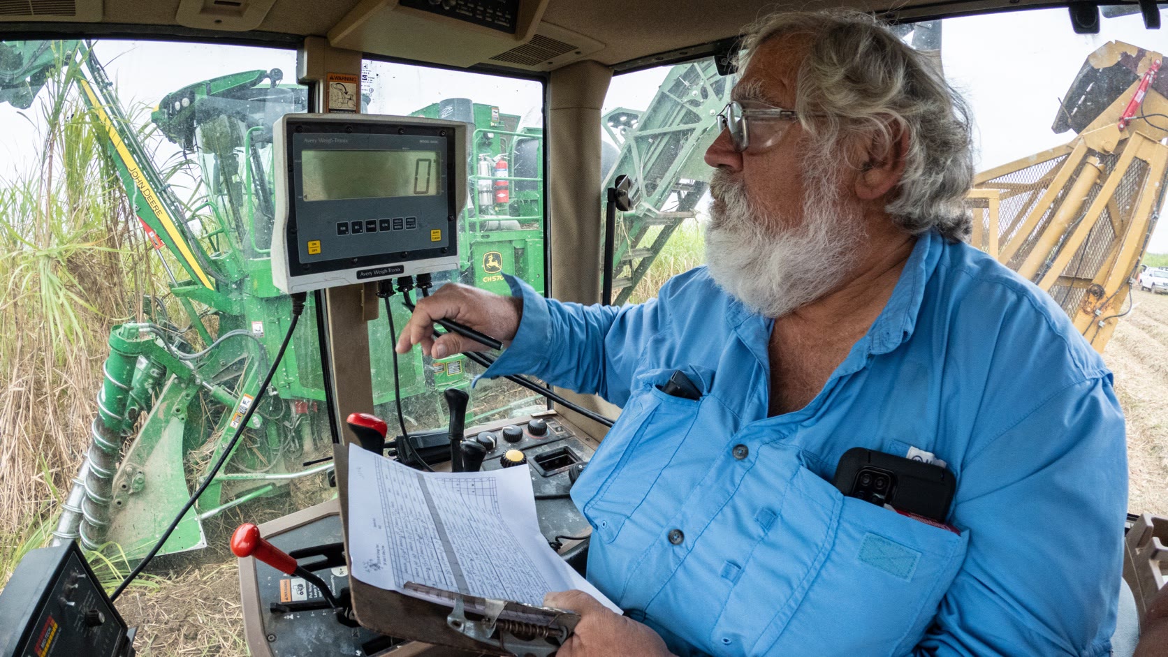 Real agricultural researcher operating machinery from a tractor cab beside a rugged mounted display