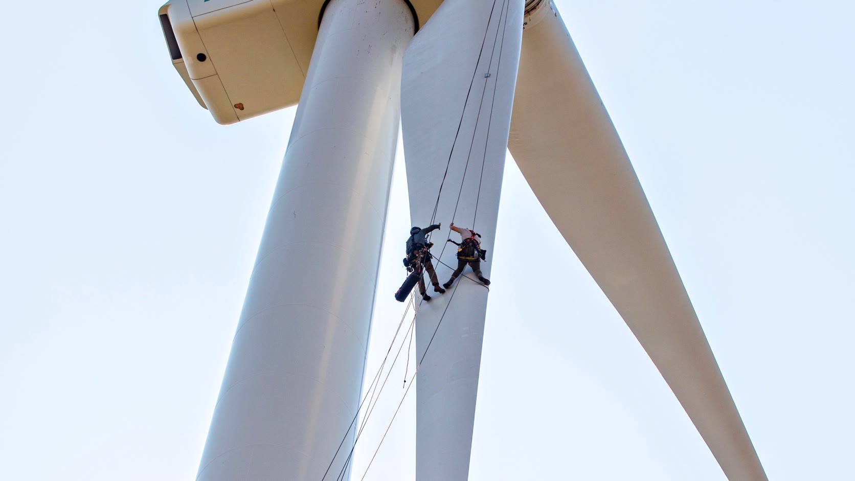 Real wind turbine maintenance technicians working on ropes near the nacelle and blades